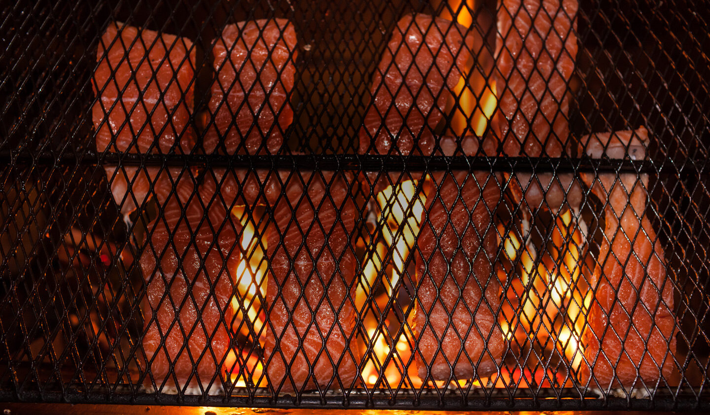 Salmon fillets cooking in metal frames over an open fire